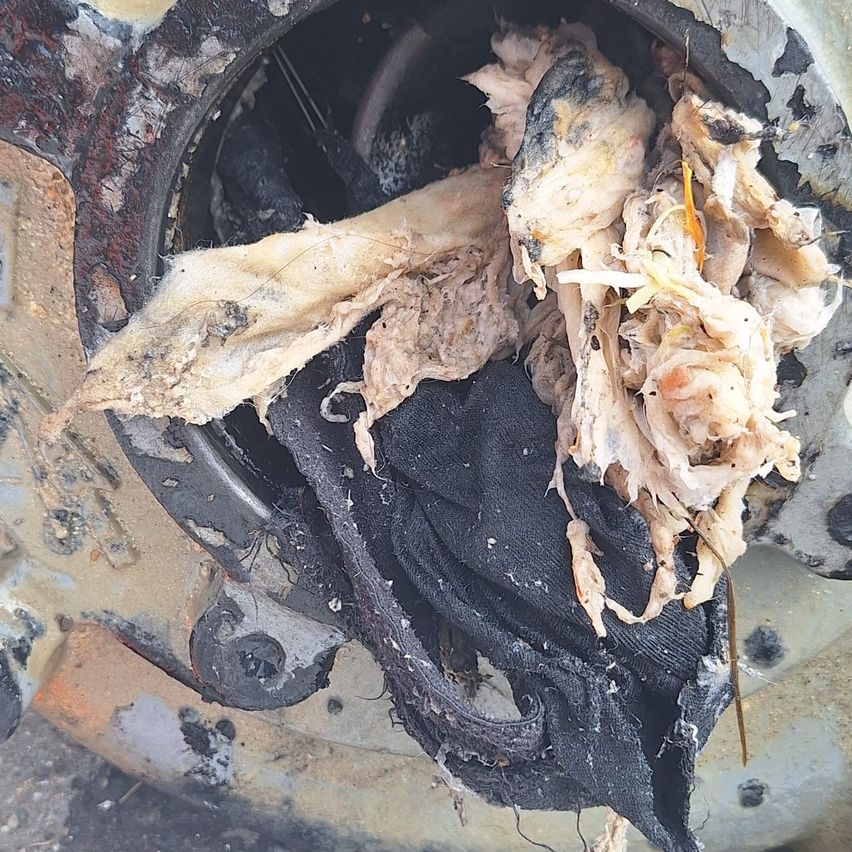 A close-up view of a burnt and charred piece of meat, possibly chicken, lying on a black cloth with a rusty metal object in the background.