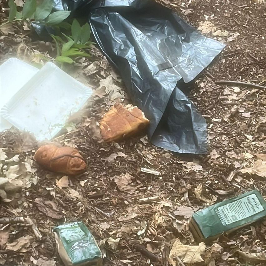Ein verschmutzter Plastiksack, zwei Croissants und einige leere Behälter liegen auf dem Boden.