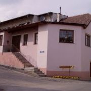 Ein rosafarbenes Haus mit einem braunen Dach und Stufen, die zum Eingang führen, am Straßenrand gelegen.