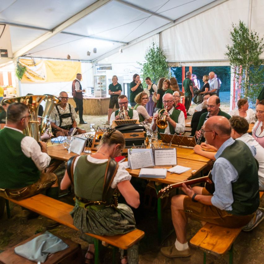 Eine Gruppe von Musikern, darunter eine Frau in einem grünen Kleid, spielt in einem Zelt mit einem Holztisch und Musikinstrumenten.