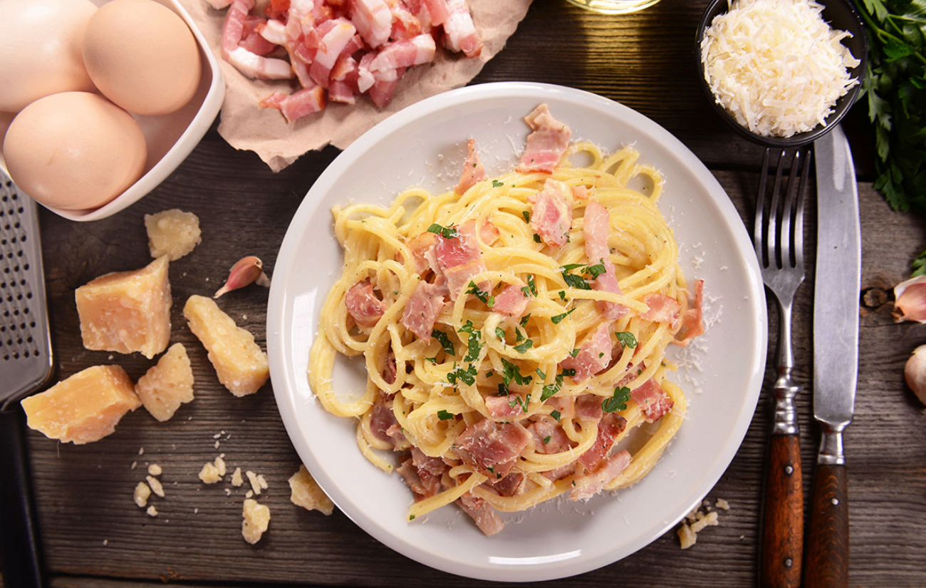Ein Teller mit Pasta, überzogen mit knusprigem Speck und mit Petersilie garniert, serviert auf einem Holztisch.