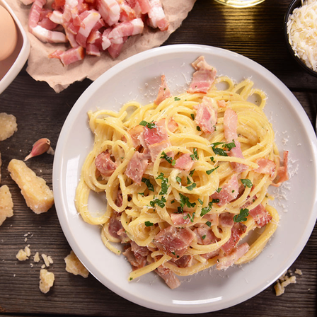 Ein Teller mit Pasta, überzogen mit knusprigem Speck und mit Petersilie garniert, serviert auf einem Holztisch.