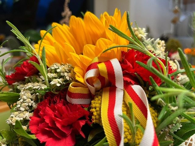 Ein Blumenstrauß mit roten, gelben und weißen Blumen und einer rot-gelben Schleife in der Mitte.