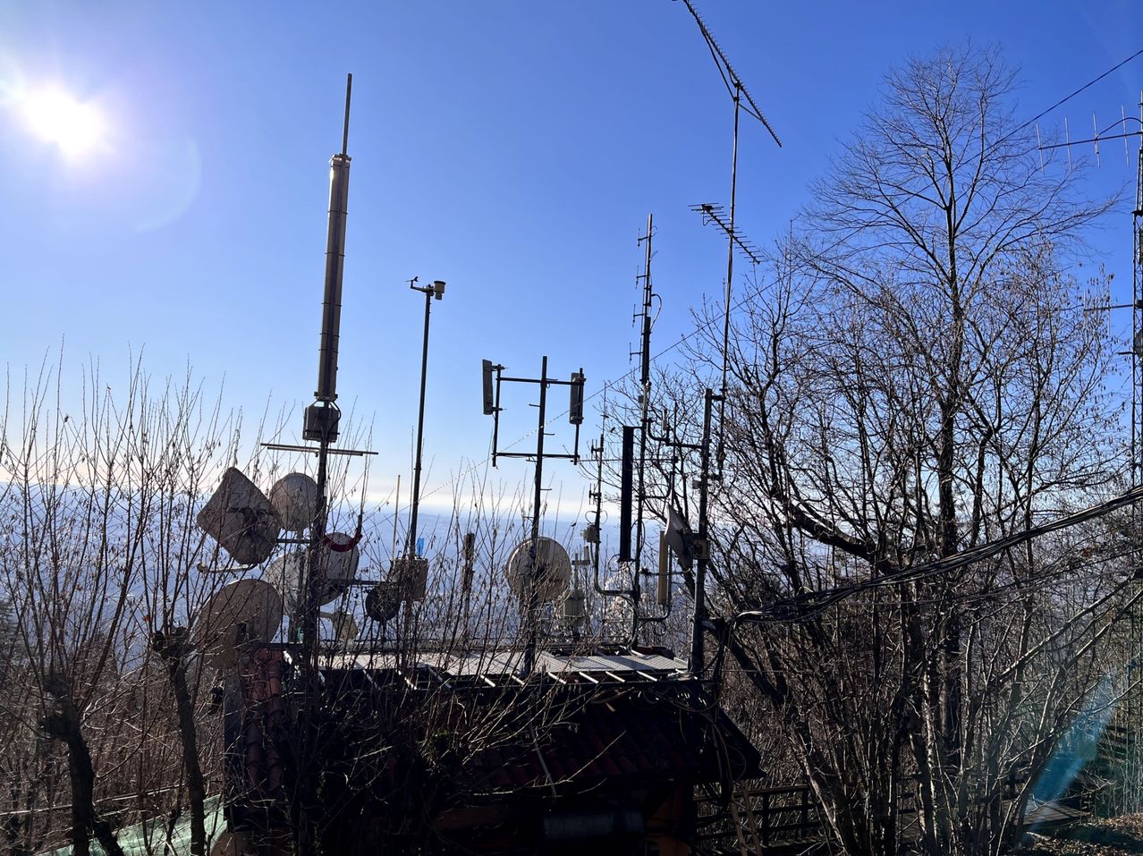 Eine Satellitenschüssel und Antennen sind auf einem Dach montiert, umgeben von Bäumen unter einem klaren blauen Himmel.