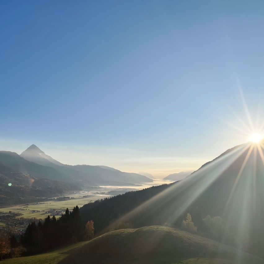 Ein atemberaubender Blick auf den Sonnenaufgang über einem Tal mit Bergen und Bäumen, der ein goldenes Licht auf die Landschaft wirft.