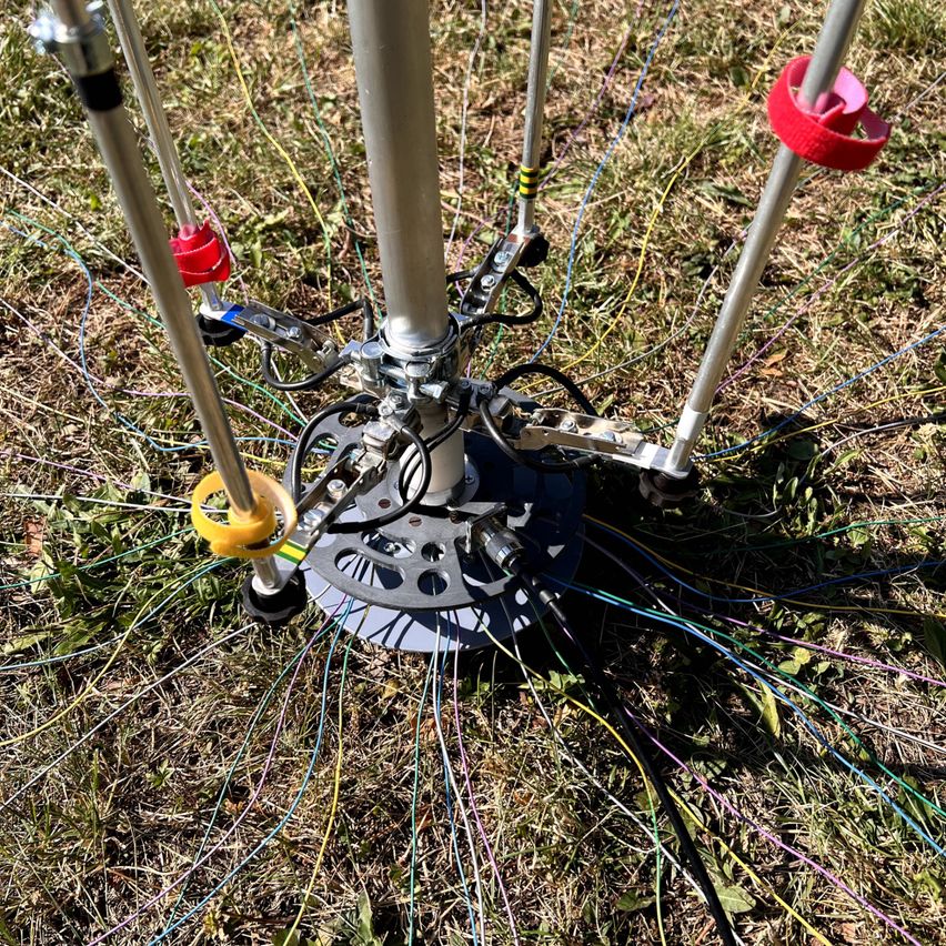 Eine Nahaufnahme einer metallischen Struktur mit mehreren Drähten und Kabeln, die darauf angeschlossen sind, auf einem Grasfeld platziert.