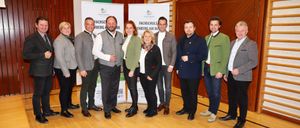 Eine Gruppe von Menschen in formeller Kleidung posiert für ein Foto vor einem Banner in einem Raum.