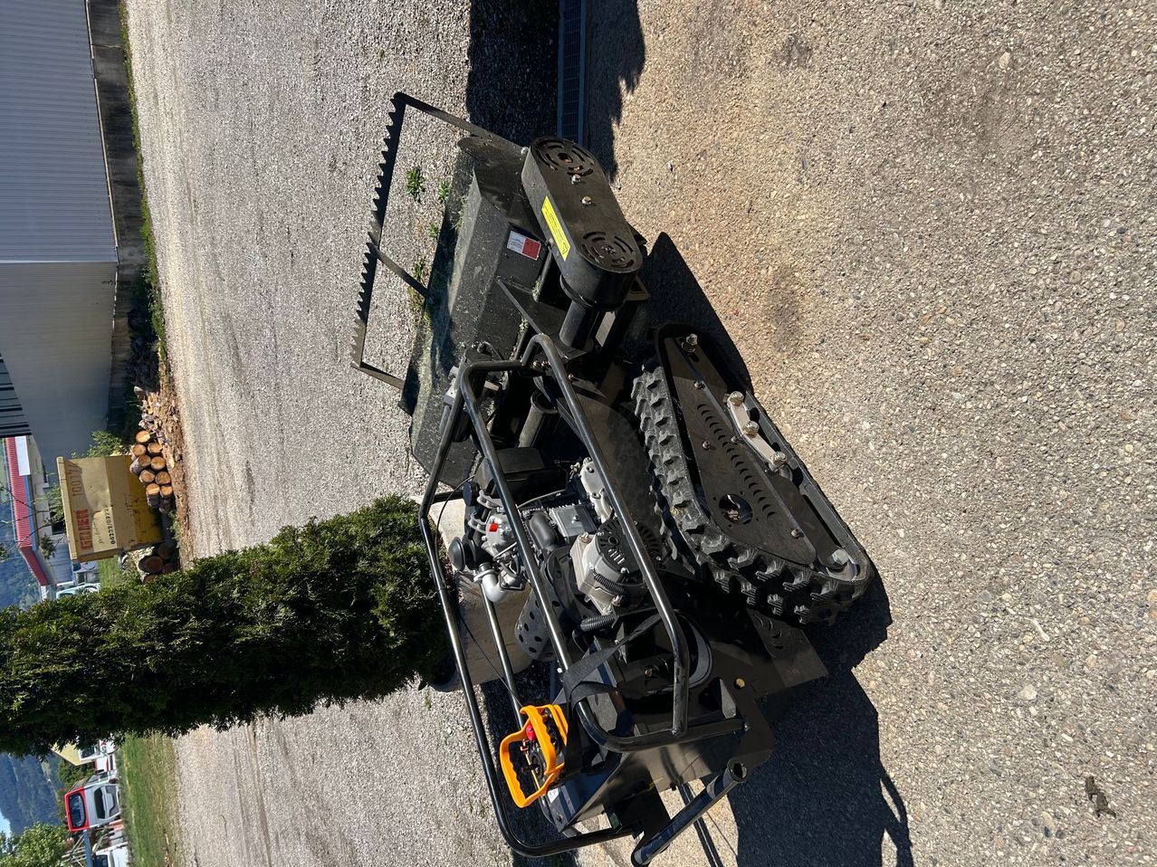 An aerial view of a black vehicle with a metal structure and a large tire on a gravel road.