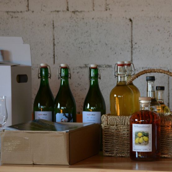 Ein Regal mit Flaschen mit Likör und Wein, eine davon Williamsbrand, ein kleiner Korb und eine Schachtel mit einer Zeitschrift darauf.