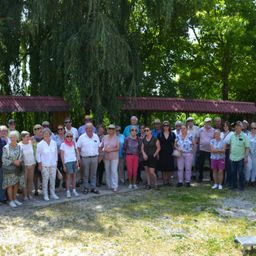 Eine Gruppe von Menschen in Sonnenbrillen und Hüten steht draußen, mit Bäumen und roten Dächern im Hintergrund. Einige tragen Brillen, Schals und Armbänder. Sie sind wahrscheinlich auf einer Klassenfahrt.