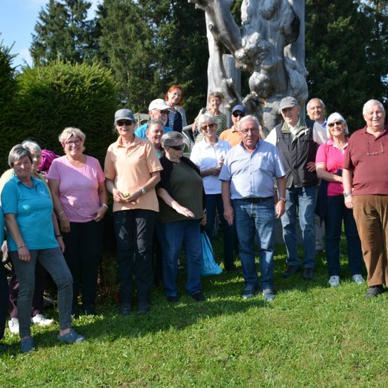 Eine Gruppe von Menschen steht vor einer großen Skulptur in einem Park. Sie lächeln und scheinen für ein Foto zu posieren.