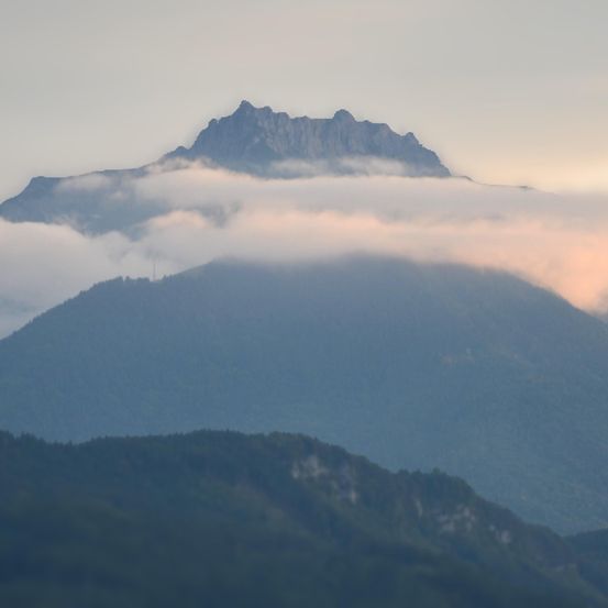 Ein nebliger Bergzug mit einem nebligen Gipfel, getaucht in ein sanftes, rosa Licht der untergehenden Sonne.