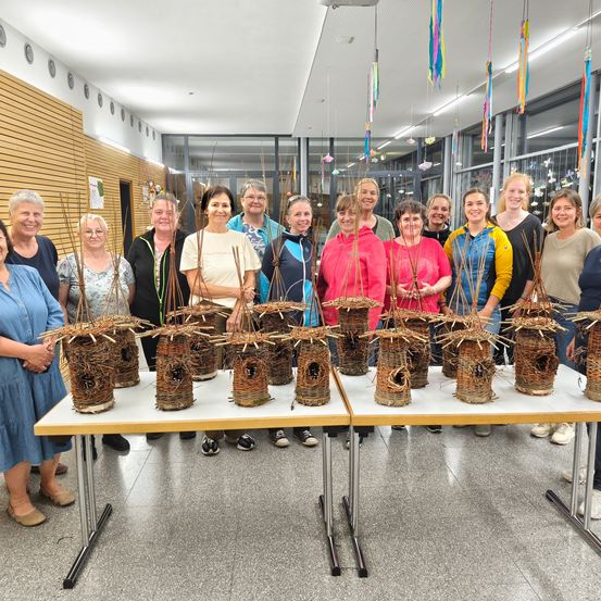 Eine Gruppe von Frauen posiert mit selbstgemachten Vogelhäuschen auf einem Tisch. Der Raum hat ein modernes Design mit Glaswänden und Dekorationen.