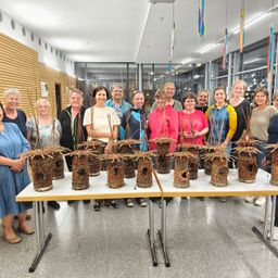 Eine Gruppe von Frauen posiert mit selbstgemachten Vogelhäuschen auf einem Tisch. Der Raum hat ein modernes Design mit Glaswänden und Dekorationen.