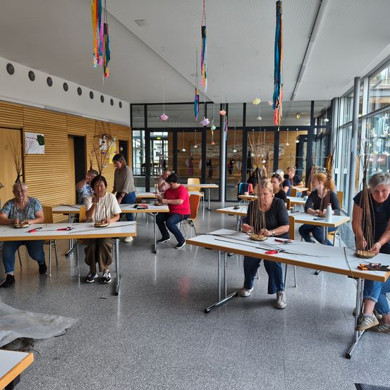 Eine Gruppe von Menschen in einem Workshop-Umfeld, die in einer Aktivität an Tischen mit verschiedenen Werkzeugen beschäftigt sind. Der Raum verfügt über Holzwände und hängende Dekorationen.