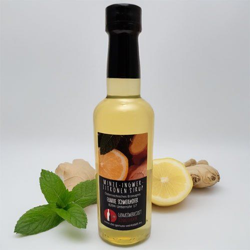 Eine Flasche Minz-Ingwer-Sirup mit schwarzem Verschluss und einer Zitronenscheibe und Ingwer und Minzblätter in der Nähe.