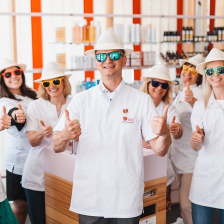 Eine Gruppe von Menschen in weißen Laborkittel und Hüten zeigt Daumen hoch in einem Salon.