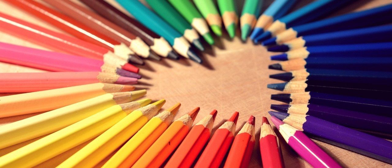 Eine kreisförmige Anordnung von Buntstiften, die eine Farbpalette zeigen, liegt auf einer Holzoberfläche. Die Stifte sind ordentlich ausgerichtet und bilden eine lebhafte und organisierte Präsentation.