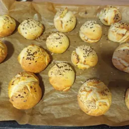 Ein Blech mit goldbraunen, mit Samen besetzten Brötchen auf Pergamentpapier, bereit zum Backen.