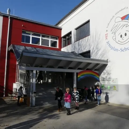 Der Eingang zu einer Schule mit einem Regenbogen an der Wand und Kindern, die draußen stehen.