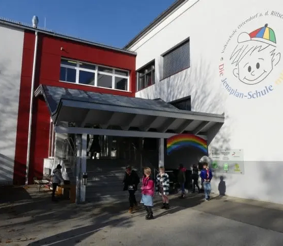 Der Eingang zu einer Schule mit einem Regenbogen an der Wand und Kindern, die draußen stehen.