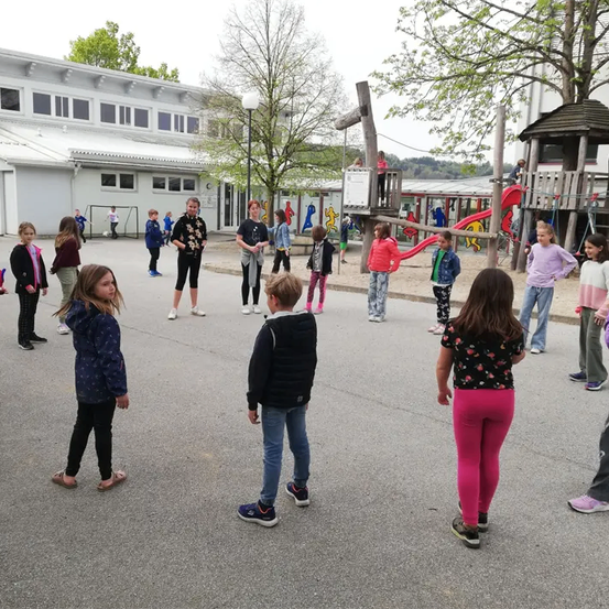 Eine Gruppe von Kindern versammelt sich auf einem Spielplatz mit einer Rutsche und einem Baumhaus, einige stehen in der Nähe eines weißen Gebäudes.