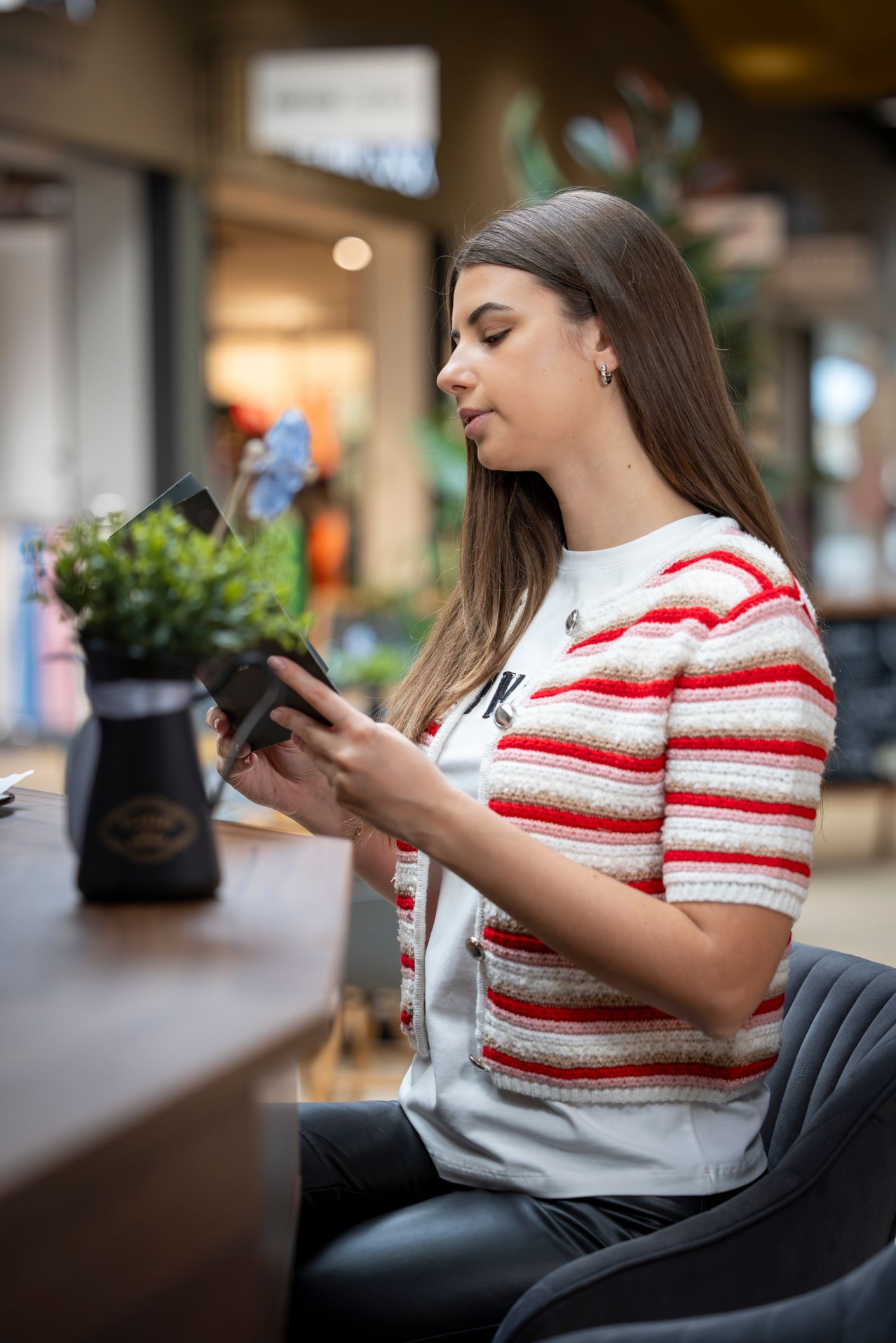 Eine Frau in einem rot-weiß gestreiften Strickjäckchen betrachtet eine Pflanze in einem Einkaufszentrum.