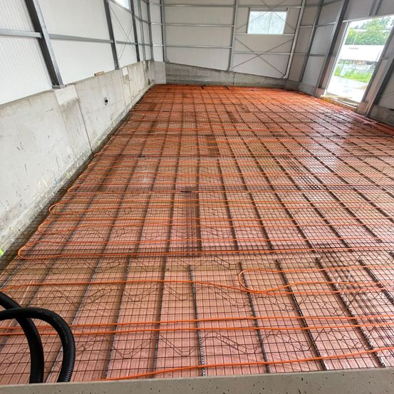 Ein leerer Raum mit rot-orangen Bodenfliesen und einem Stahlrahmen. Der Raum hat weiße Wände und Metallstrukturen sowie eine Tür in der Mitte.