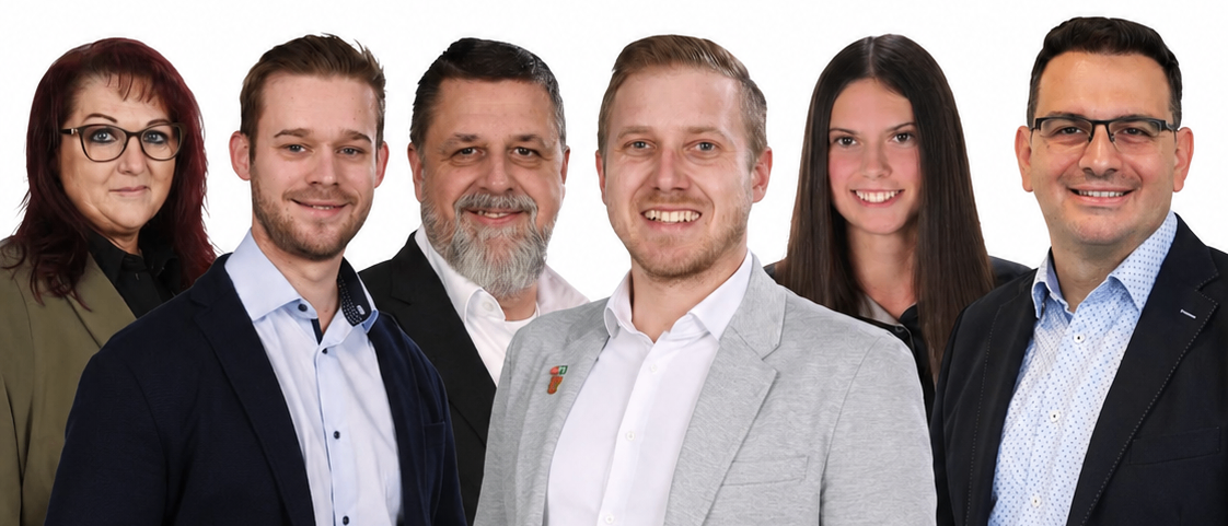 Eine Gruppe von sechs Personen, alle lächelnd, stehen in einem Studio zusammen. Sie sind formell gekleidet.