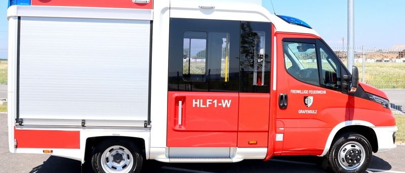Ein rot-weißes Notfallfahrzeug mit der Bezeichnung HLF1-W in einem Parkplatz geparkt.