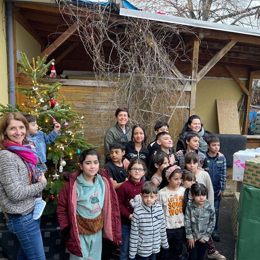 Eine Gruppe von Kindern und Erwachsenen steht draußen. Die Kinder tragen Winterkleidung und lächeln. Sie stehen vor einem geschmückten Weihnachtsbaum.