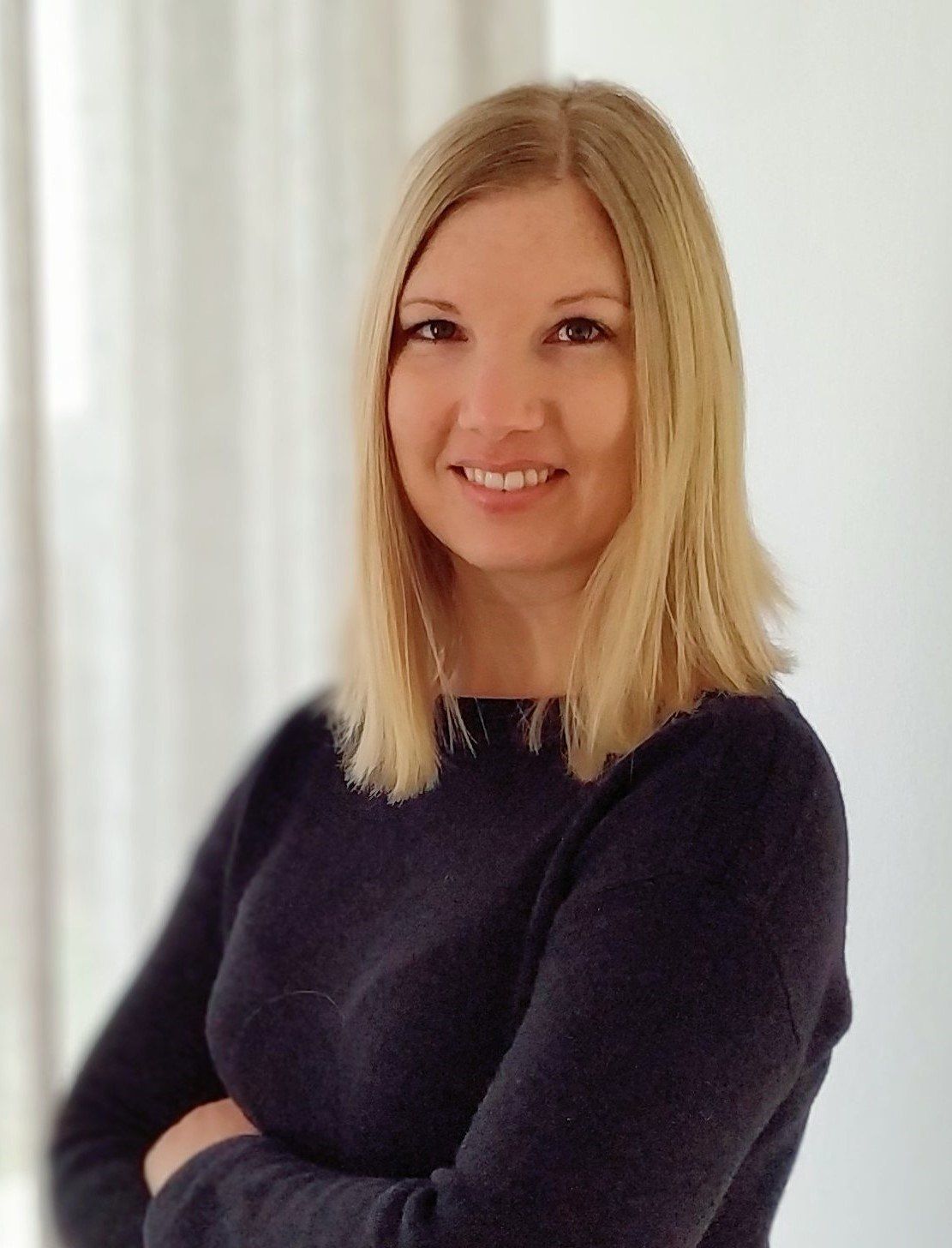 Eine Frau mit blonden Haaren, die ein dunkelblaues Sweatshirt trägt und in die Kamera lächelt.