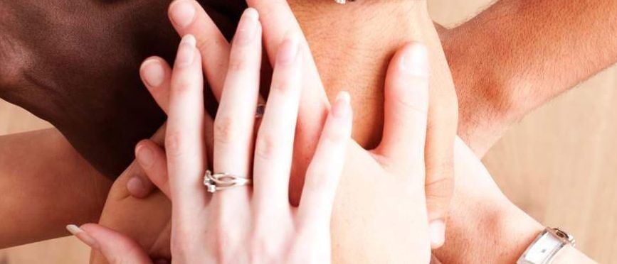 Vier Menschen halten sich an den Händen, drei tragen Armbänder und einer eine Uhr.