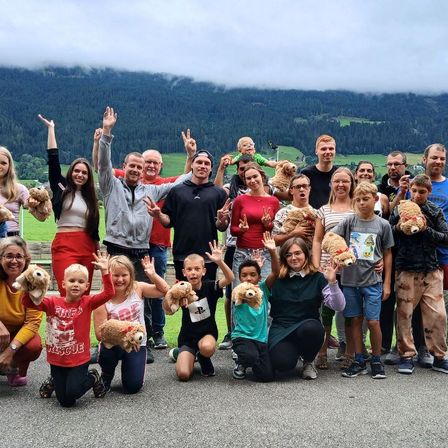 Eine Gruppe von Menschen macht ein Foto in einem Gebirgsgebiet. Sie tragen alle verschiedene Kleidung und halten Plüschtiere.