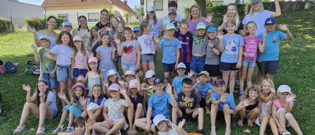 Eine Gruppe von Kindern und Erwachsenen posiert für ein Foto im Garten, einige sitzen und andere stehen, mit Häusern im Hintergrund.