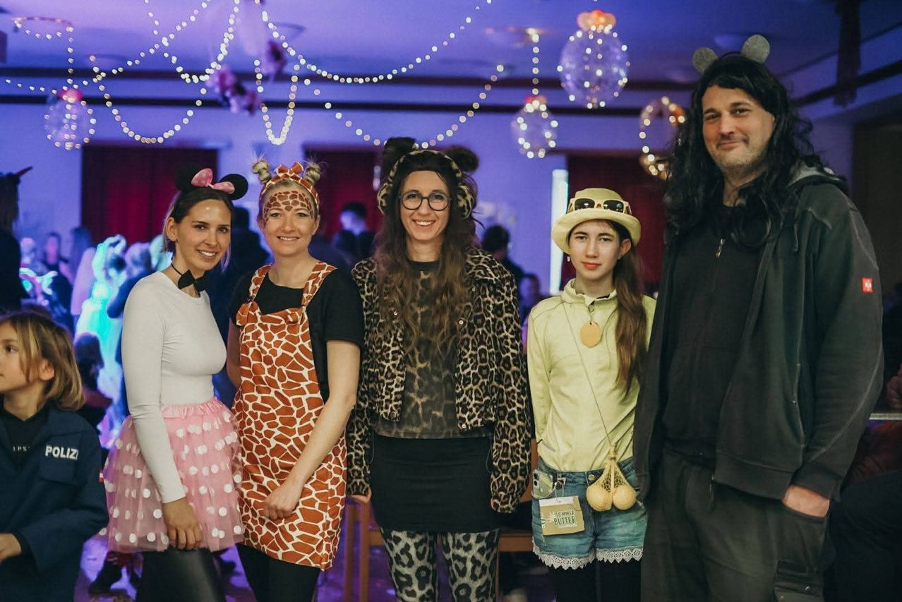 Eine Gruppe von Erwachsenen und einem Kind in Tierkostümen und Mickey-Mouse-Ohren posiert für ein Foto in einem dekorierten Raum.