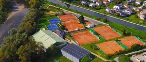 Eine Luftaufnahme einer Gemeinde mit Tennisplätzen, Häusern und einem Fluss. Das Gebiet hat grüne Felder, Bäume und einen Gehweg.