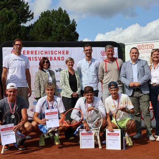 Eine Gruppe von Tennisspielern und Offiziellen posiert für ein Foto auf einem Tennisplatz mit Hintergrund. Die Spieler halten Schläger und haben Medaillen um den Hals. Ein Banner hinter ihnen lautet 'Osterreichischer Tennisverband'.