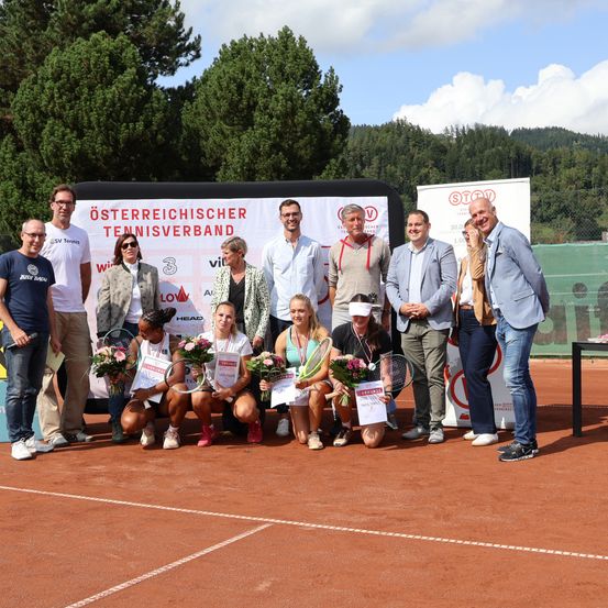 Tennisspieler posieren für ein Foto auf einem Tennisplatz mit einem Hintergrund, auf dem 'Osterreichischer Tennisverband' steht. Einige halten Blumen und Pokale.