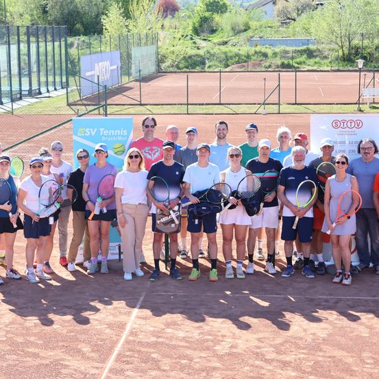 Eine Gruppe von Tennisspielern auf einem Tennisplatz, mit Schlägern, in Reihen stehend, mit einem Banner und Zaun im Hintergrund.