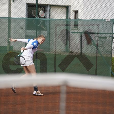 Eine junge Frau spielt Tennis auf einem Sandplatz, hält einen Tennisschläger und springt, um den Ball zu schlagen.