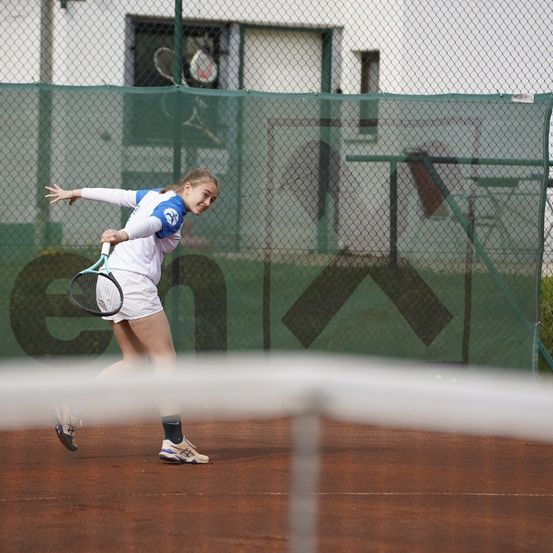 Eine junge Frau spielt Tennis auf einem Sandplatz, hält einen Tennisschläger und springt, um den Ball zu schlagen.