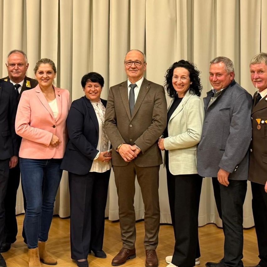 A group of people dressed in formal attire, possibly officials, are standing together and smiling for a photo in front of a curtain.