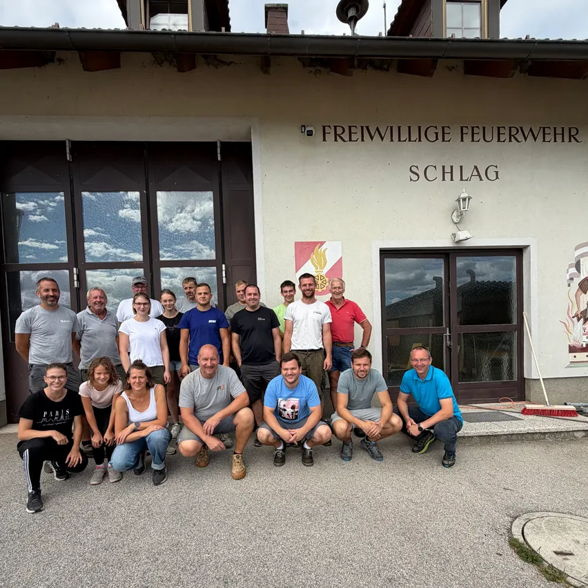 Eine Gruppe von Menschen in Freizeitkleidung posiert für ein Foto vor einem Gebäude mit der Aufschrift Freiwillige Feuerwehr Schlag.