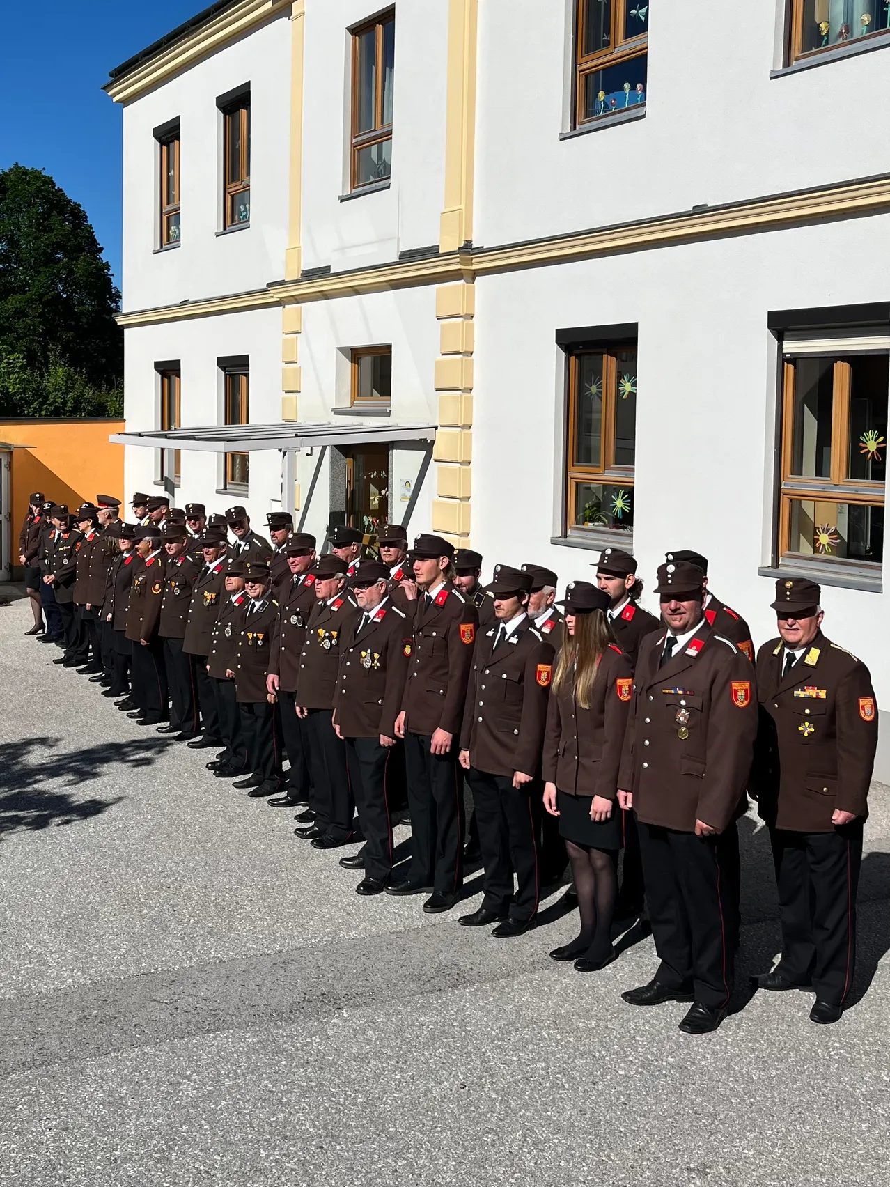 Eine Reihe uniformierter Personen steht vor einem weißen Gebäude mit gelben Akzenten und großen Fenstern.