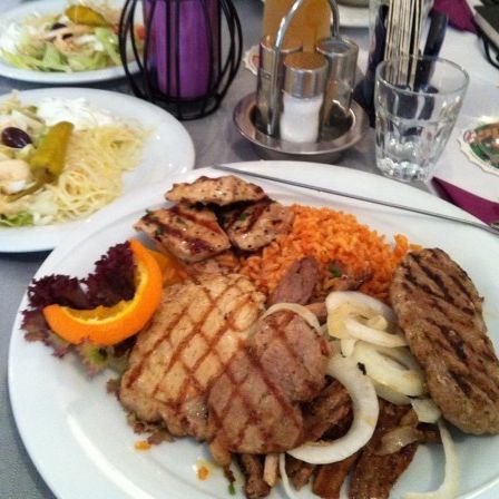 Zwei Teller mit Essen, einer mit gegrilltem Fleisch, Reis, Zwiebeln und Orange, der andere mit Salat und Dressing.