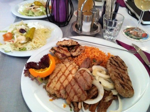 Zwei Teller mit Essen, einer mit gegrilltem Fleisch, Reis, Zwiebeln und Orange, der andere mit Salat und Dressing.