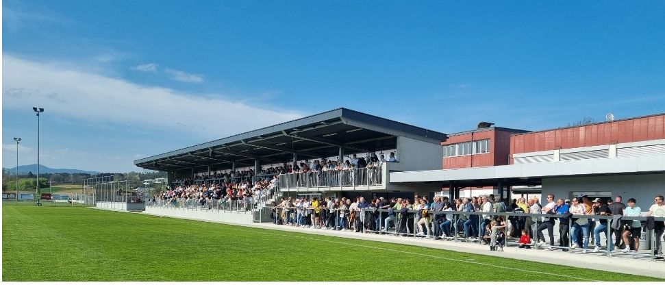 Eine Menschenmenge steht auf den Geländern eines Stadions und sieht sich ein Spiel auf dem Spielfeld an.