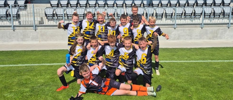 Die U11-Fußballmannschaft feiert ihre erfolgreiche Saison auf dem Feld, umgeben von Trophäen.
