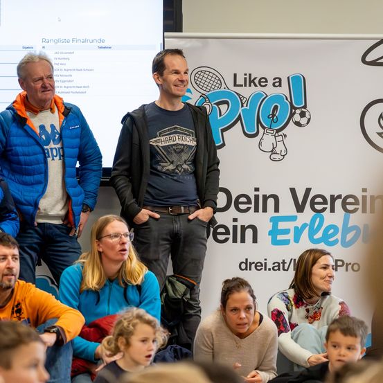 Eine Gruppe von Menschen steht vor einer Tafel und lächelt für ein Foto. Auf der Tafel steht 'Like a Pro'. Ein Mann steht mit den Händen in den Taschen.